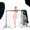 Fashion model posing elegantly in a studio with modern lighting setup and chic clothing.