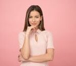Portrait of a young woman posing elegantly in a studio with a pink background.