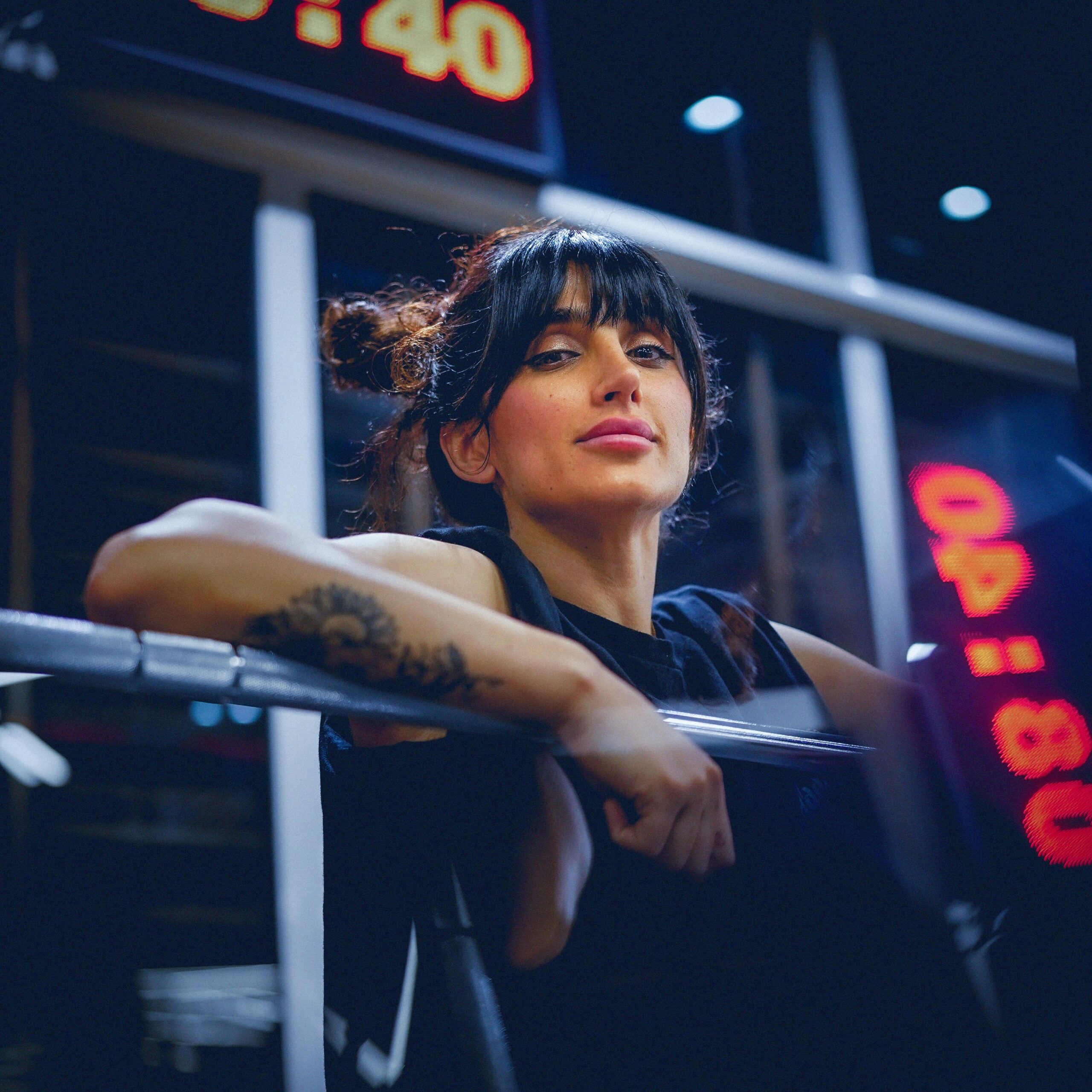 A youthful woman poses confidently in a gym, surrounded by fitness equipment.